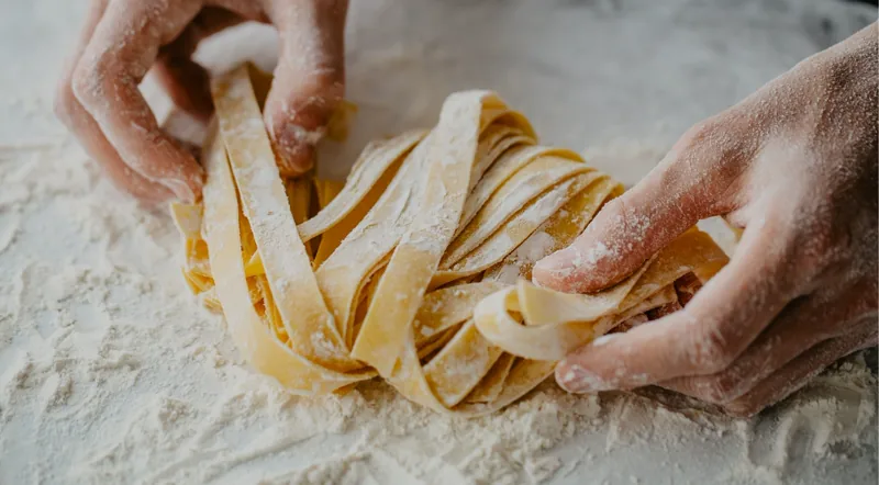 Hands rolling fresh fettuccine ribbons in flour