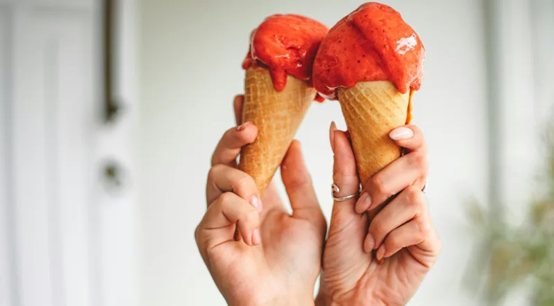 Two hands holding strawberry gelato cones in Rome