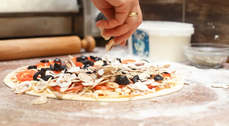 Adding mushrooms and olives to a pizza base at a Rome pizza class