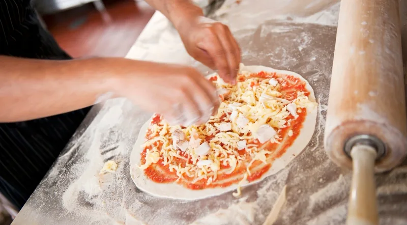 Topping a hand-stretched Roman-style pizza with cheese